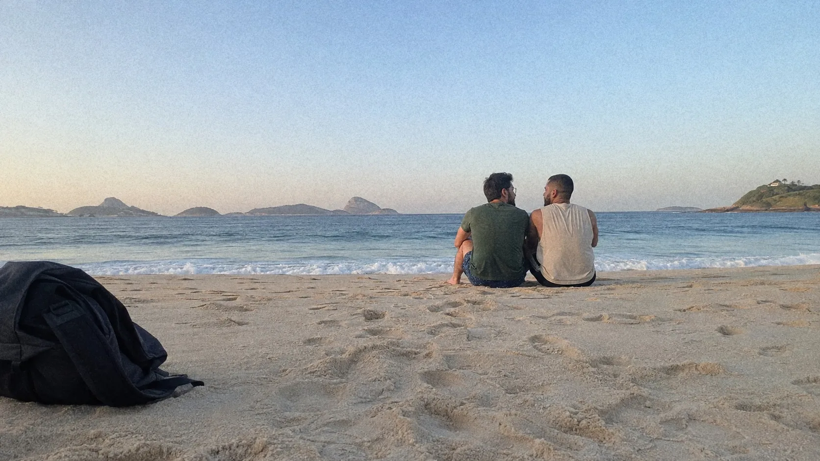 Two people sitting together on the sand, facing the sea.