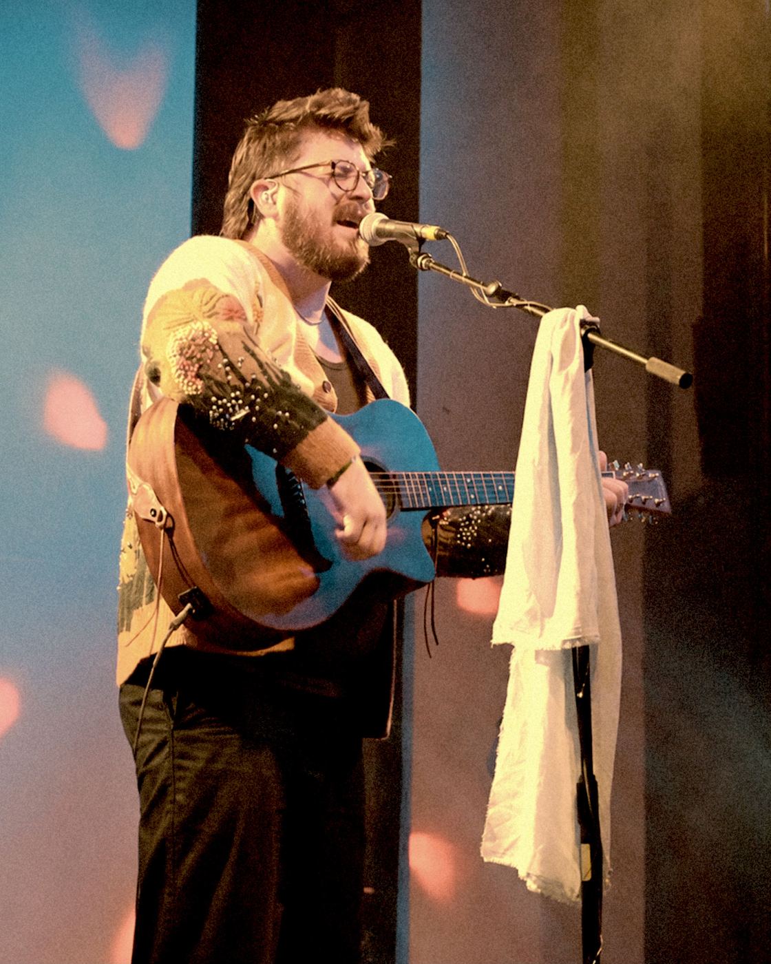 Spencer Sanders on stage, singing into a microphone with his guitar